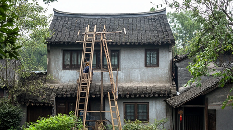 工人在古旧房屋外使用竹梯作业