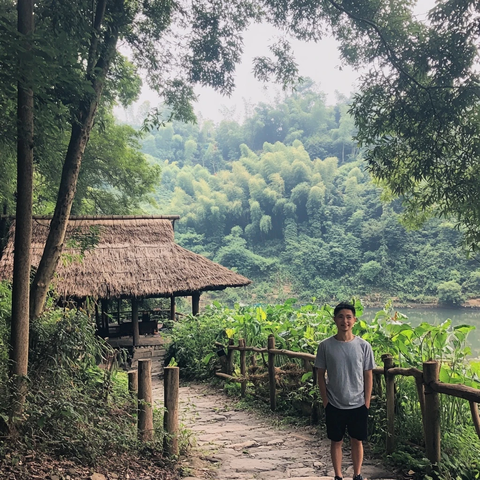 男子站在山林小屋旁的石板路上